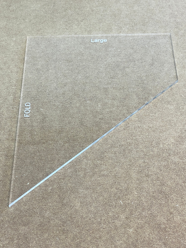 May include: A clear plastic ruler with a diagonal fold line. The ruler is labeled "Large" and "FOLD".