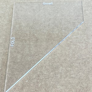 May include: A clear plastic triangle ruler with the word "FOLD" printed vertically on the left side and "Small" printed horizontally near the top.