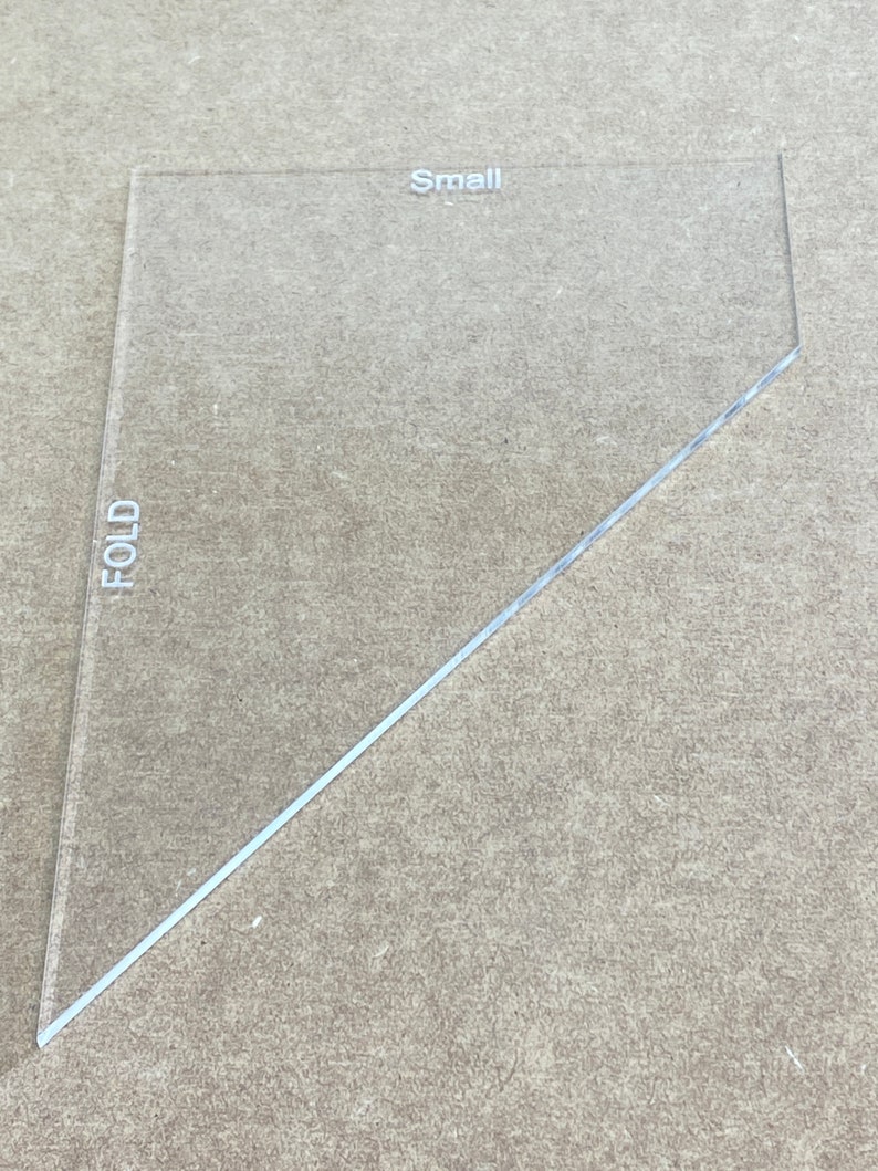 May include: A clear plastic triangle ruler with the word "FOLD" printed vertically on the left side and "Small" printed horizontally near the top.