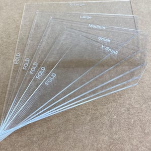 May include: Six clear plastic sheets with the words "FOLD" printed on the side. The sheets are labeled with different sizes: X-Large, Large, Medium, Small, and X-Small.