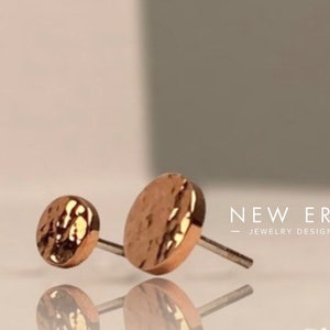 Pode incluir: Dois brincos de pressão de ouro rosa com textura martelada. Os brincos são pequenos e redondos, e têm um design simples e minimalista.