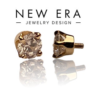 May include: A pair of gold-toned body jewelry with a clear gemstone in a prong setting. The jewelry is threaded with a screw-on back.