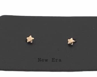 May include: A pair of gold star-shaped stud earrings displayed on a black card with the text "New Era".