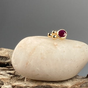 May include: A gold nose stud with a small ruby gemstone and three gold beads.