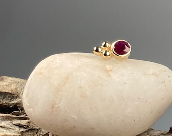May include: A gold nose stud with a small ruby gemstone and three gold beads.