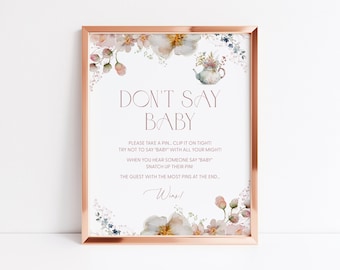 May include: A framed sign with the text "DON'T SAY BABY" in a soft pink hue. The sign includes instructions for a baby shower game, surrounded by floral watercolor illustrations in shades of pink, white, and gold. The frame is a rose gold colour.
