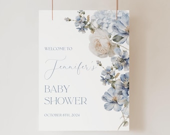May include: A rectangular sign with a white background featuring blue and cream watercolor floral illustrations on the right side. The text reads: WELCOME TO Jennifer's BABY SHOWER OCTOBER 8TH, 2024 in blue serif and script fonts.