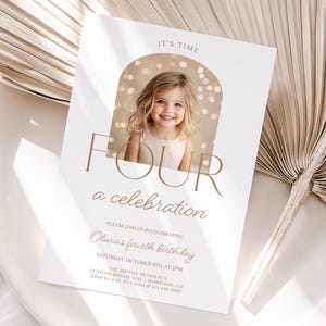 Puede incluir: Una tarjeta de invitación blanca con letras doradas anunciando una fiesta de cumpleaños de cuarto año. La tarjeta presenta una foto de una niña con un vestido blanco bajo un arco dorado con luces brillantes. El texto dice "It's Time Four a Celebration" e incluye la fecha, la hora y la ubicación de la fiesta.