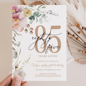 Könnte beinhalten: Einladungskarte für eine Feier zum fünfundachtzigsten Geburtstag. Das Design zeigt einen floralen Rand mit rosa und gelben Blumen und grünem Laub. Der Text enthält "fünfundachtzig" in einer stilvollen Schriftart.