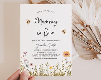 May include: A white baby shower invitation card featuring the text Let's Shower the Mommy to Bee, two small illustrated bees, and a colorful floral border at the bottom with various wildflowers in shades of yellow, pink, and green.