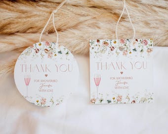 May include: Two white gift tags, one circular and one square, featuring a floral border, a pink champagne flute illustration, and the text THANK YOU FOR SHOWERING Jennifer WITH LOVE. Each tag has a white string attached for hanging.
