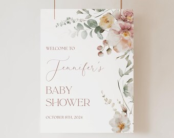 May include: A white rectangular sign featuring floral illustrations in shades of pink, yellow, and green. The text reads: WELCOME TO Jennifer's BABY SHOWER OCTOBER 8TH, 2024. The floral arrangement is positioned along the top and right edges.