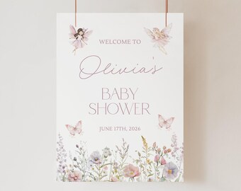 May include: A white rectangular baby shower welcome sign featuring the text Welcome to Olivia's Baby Shower June 17th, 2026. The design includes two illustrated fairies, two butterflies, and a bottom border of watercolor wildflowers.
