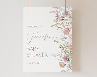 May include: A white rectangular sign featuring the text WELCOME TO Jennifer's BABY SHOWER JUNE 17TH, 2024 in dark pink lettering. The right side of the sign is decorated with a watercolor illustration of various wildflowers in pink, purple, and green.