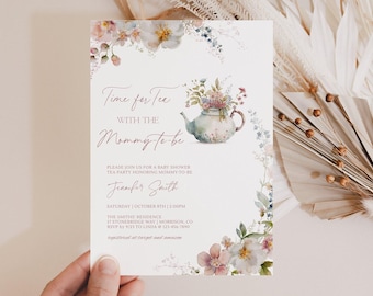 May include: A baby shower invitation with a floral watercolour design. The invitation reads "Time for Tea with the Mommy-to-be" and includes event details. A teapot illustration is featured, surrounded by flowers. The invitation is held by a hand.