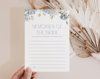 Op de afbeelding: Een witte kaart met de tekst "MEMORIES OF THE BRIDE" in marineblauw, met een bloemenontwerp in de bovenhoeken. De kaart heeft lijnen om op te schrijven en de tekst "SHARE YOUR FAVORITE MEMORY OF THE BRIDE-TO-BE".