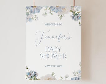 May include: A rectangular sign with a white background featuring watercolor blue and white flowers at the top and bottom corners. The text reads: WELCOME TO Jennifer's BABY SHOWER MAY 18TH, 2026 in blue lettering with a mix of serif and script fonts.