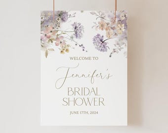 May include: A rectangular sign with a white background featuring watercolor floral illustrations in shades of purple, pink, and yellow. The text reads: WELCOME TO Jennifer's BRIDAL SHOWER JUNE 17TH, 2024 in a mix of serif and script fonts.