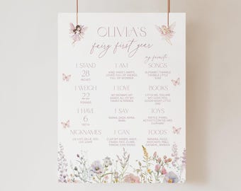 May include: A white milestone poster titled Olivia's fairy first year, featuring illustrations of fairies and butterflies. It lists developmental details including 28 inches, 22 pounds, 6 teeth, and various personal favorites, finished with a floral border.
