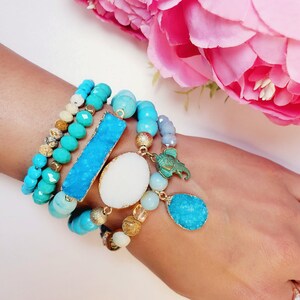 May include: A stack of turquoise and blue beaded bracelets with a large turquoise stone, a white stone, and a small elephant charm.