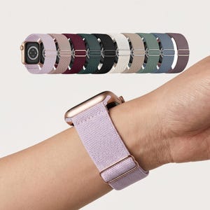 May include: A collection of Apple Watch bands in various colors, including lavender, burgundy, and black. The bands are made of a woven material and are displayed on a white background. One band is shown worn on a wrist.