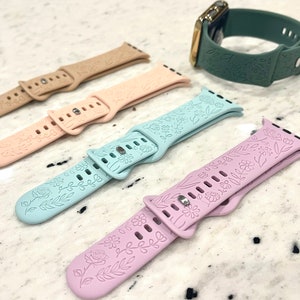 Op de afbeelding: Vier verschillende gekleurde horlogebandjes met bloemenmotieven. De bandjes zijn gemaakt van siliconen en zijn compatibel met de Apple Watch.