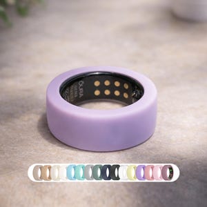 May include: A lavender-colored Oura ring, a wearable health tracker, is displayed. The ring has a smooth, rounded design with a black interior featuring sensors. A selection of ring colors is shown below. The ring is a health and fitness accessory.