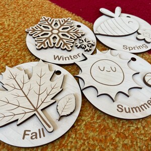 May include: Wooden seasonal learning toys. The set includes four wooden discs, each representing a season: Winter with a snowflake, Spring with a bee, Summer with a sun, and Fall with a leaf. Each disc has the season's name engraved.