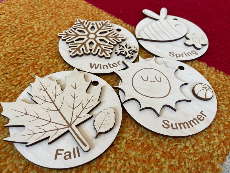 May include: Wooden seasonal learning toys. The set includes four wooden discs, each representing a season: Winter with a snowflake, Spring with a bee, Summer with a sun, and Fall with a leaf. Each disc has the season's name engraved.
