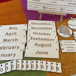 May include: Wooden educational calendar set with months, days, numbers, and seasonal icons. Includes month and day labels, numbers 0-9, and seasonal icons for Winter, Spring, and Fall. The calendar is designed for educational purposes.
