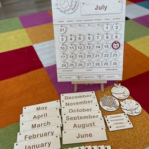May include: A wooden perpetual calendar with interchangeable month, date, and season pieces. The calendar displays the month of July, the year 2022, and the date of the 16th. Includes wooden numbers, months, days of the week, and seasonal icons.