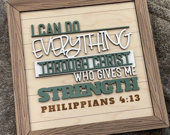 May include: Wooden framed sign with the words "I CAN DO EVERYTHING THROUGH CHRIST WHO GIVES ME STRENGTH PHILIPPIANS 4:13". The text is in various colors, including white, green, and brown, on a light wood background.