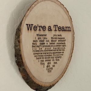 May include: A wooden plaque with a natural bark edge. The text "We're a Team" is at the top, with a poem below. The poem includes phrases like "I got you" and "I love you", making it a sentimental gift.