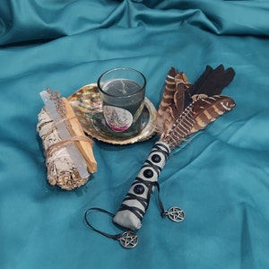 Può includere: Un bastoncino di salvia bianca, un ventaglio di piume bianco e nero, un portacandele di vetro con una candela nera e una conchiglia con un ciondolo pentagramma.