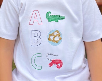 Camiseta de regreso a clases del abecedario de Luisiana: Caimán cajún, beignet, cangrejo de río.
