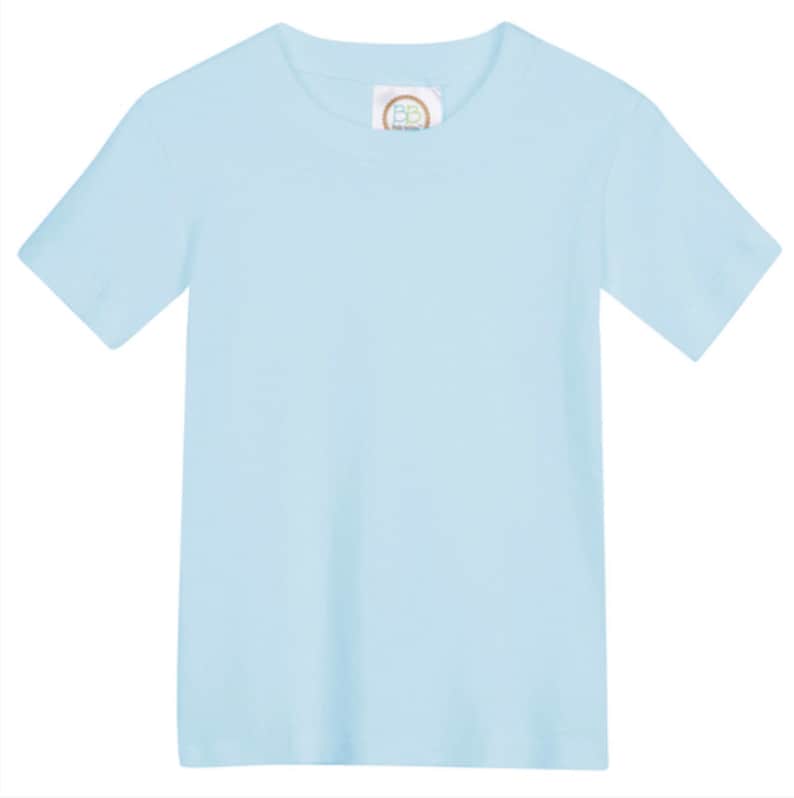 May include: A solid light blue short-sleeve t-shirt with a crew neckline. The garment features a small white interior neck label with the letters BB printed in a circular gold border, centered at the inner collar of the plain light blue shirt.