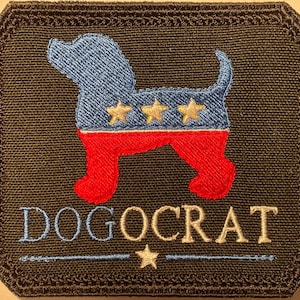 May include: Embroidered patch featuring a dog silhouette in blue and red, with three gold stars. The word "DOGOCRAT" is embroidered below the dog. The patch has a black background and a stitched border.