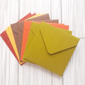May include: A stack of colorful envelopes in shades of red, orange, yellow, brown, and green. The envelopes are arranged in a fan shape, with the green envelope on top.