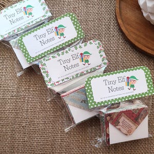 May include: Several packages of "Tiny Elf Notes" are displayed. Each package contains small, patterned envelopes. The labels feature a cartoon elf and the text "Tiny Elf Notes" in a playful font, with a green polka dot border.
