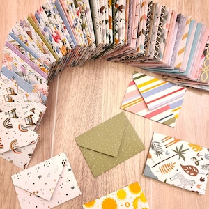 May include: A collection of colorful patterned envelopes, some with geometric designs, others with floral patterns, and some with animal prints. The envelopes are arranged in a semi-circle on a wooden surface.