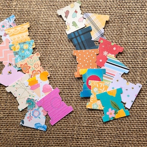 May include: A collection of colorful, patterned paper tags with a unique shape. The tags feature various designs, including floral, geometric, and food-themed patterns. The tags are arranged on a textured, brown surface.