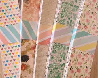 May include: A stack of patterned paper in various designs, including hearts, flowers, and text. The paper is wrapped with colorful striped tape.