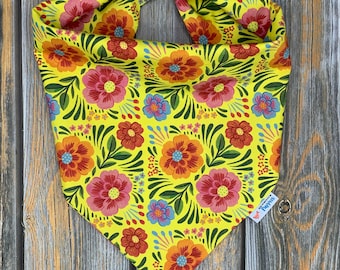May include: Yellow bandana with a floral pattern featuring red, pink, orange, and blue flowers. The bandana is tied in a knot at the top and has a small tag that says "Pawsitive Pups".