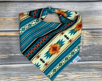 May include: A turquoise, cream, black, red and orange bandana with a Southwestern geometric pattern. The bandana is tied in a knot and has a "Custom Pups" label attached.