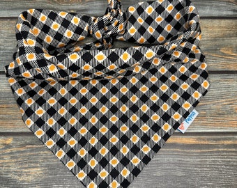 May include: Black and white bandana with a yellow and white checkered pattern. The bandana is tied in a knot and has a "Puppies" label attached.