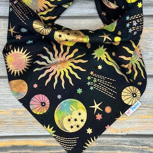 Könnte beinhalten: Schwarzes Bandana mit einem goldenen Himmelsdruck mit Sonnen, Monden und Sternen. Das Bandana ist oben zu einem Knoten gebunden und hat unten rechts den Schriftzug "Puppets" aufgedruckt.