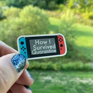 May include: A white sticker with a Nintendo Switch design. The sticker says "How I Survived Quarantine".