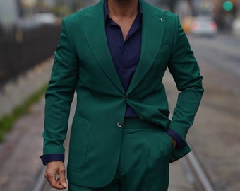 May include: A man wearing a dark green suit jacket and matching trousers. He is wearing a dark blue collared shirt underneath the jacket. He is also wearing sunglasses.