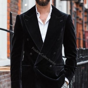 Könnte beinhalten: Ein schwarzer Samtblazer mit Doppelreiherknöpfen und einem weißen Hemd mit Kragen darunter. Der Blazer hat eine klassische Passform und verfügt über einen Doppelreiherverschluss mit Knöpfen. Der Stoff ist weich und luxuriös, und der Blazer ist perfekt für einen formellen Anlass.