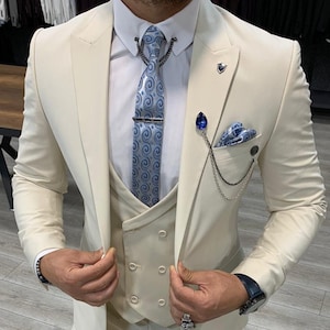 May include: A beige suit with a vest and a blue patterned tie. The suit has a double-breasted vest and a chain detail on the jacket.
